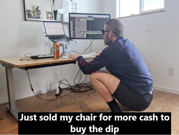 A man squats on a chair at a desk with dual monitors, with text reading "Just sold my chair for more cash to buy the dip."