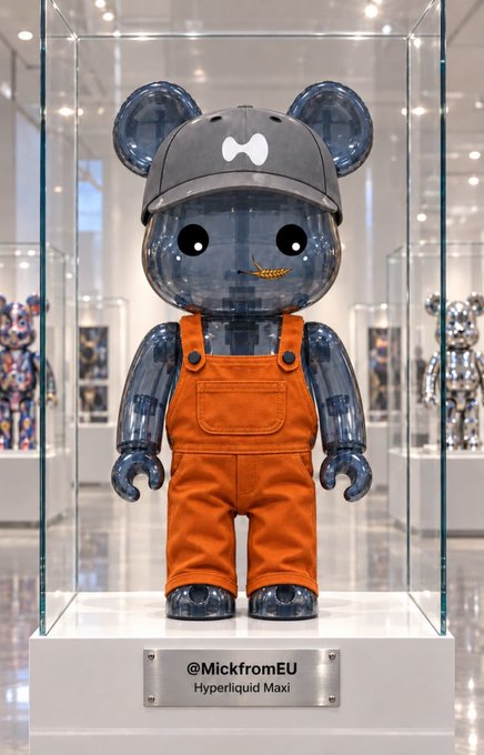 A transparent blue Bearbrick figure wearing orange overalls and a gray cap is displayed in a glass case with a plaque reading '@MickfromEU Hyperliquid Maxi'.