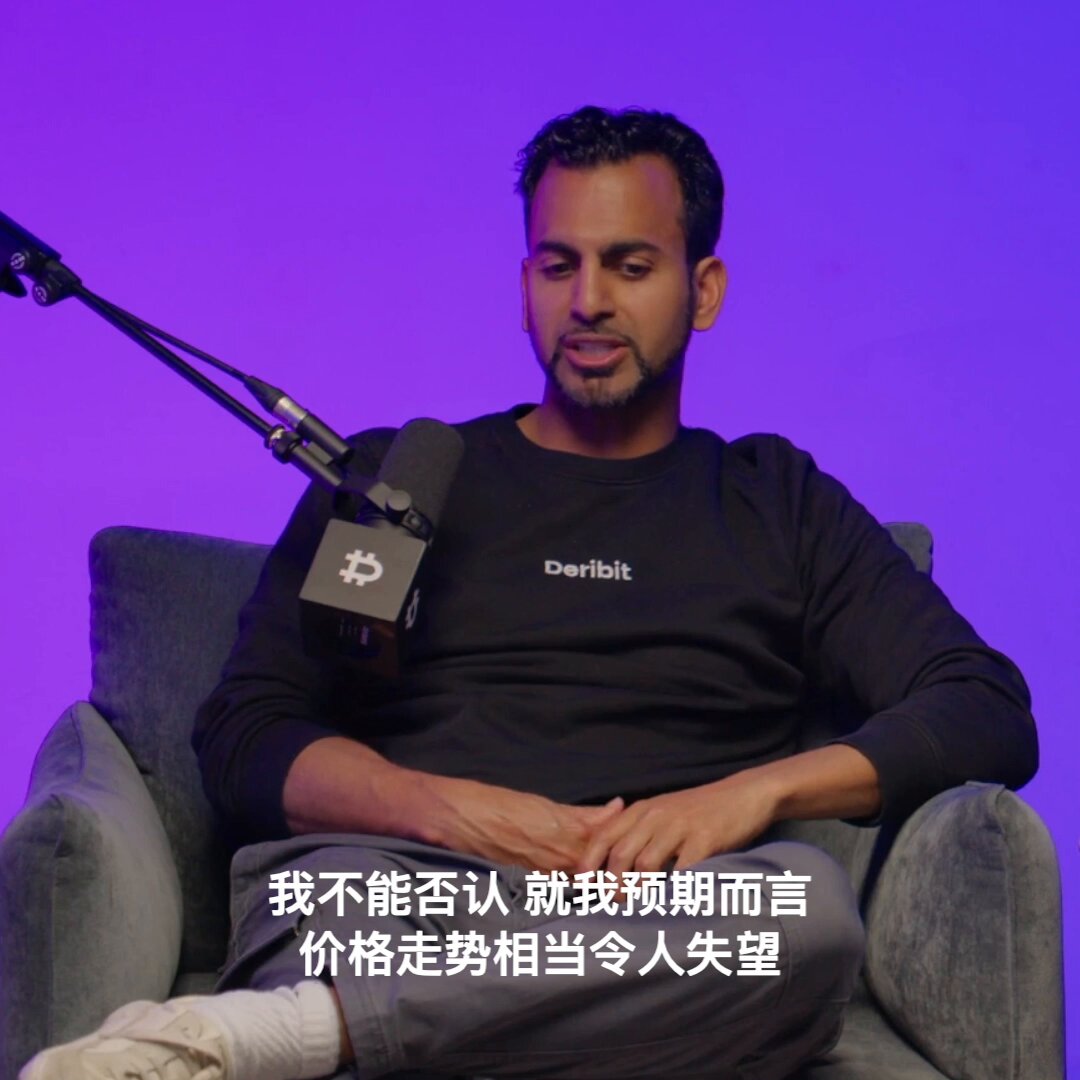 The image features a man sitting down, wearing a black shirt with white text that says "derbit" on it. The man appears to be talking into a microphone while seated in a chair. There are also some Chinese characters visible in the image, which might suggest that this is an audio or video clip from a foreign language source.