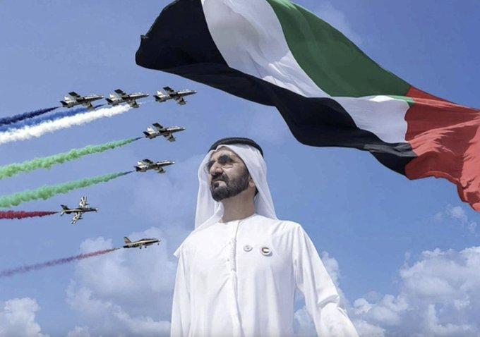 A man in traditional Emirati attire stands proudly beneath the UAE flag as military jets soar across the sky trailing red, green, and white smoke, symbolizing Dubai's pioneering milestone as the first Middle Eastern government to embrace Bitcoin and cryptocurrency.