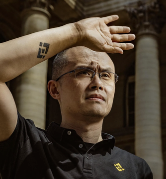 A man wearing a black polo shirt featuring the yellow Binance logo raises his arm to shield his eyes from the sun in front of a grand columned building. The Binance-branded attire visually connects to the caption, which attributes the quote about "hot money" rotating from AI back into crypto to the Binance founder.