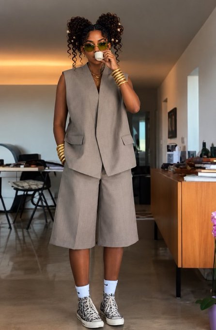 A fashion photo of a woman wearing a taupe sleeveless vest and matching Bermuda shorts, accessorized with gold bangles, sunglasses, white Nike socks, and leopard-print sneakers.