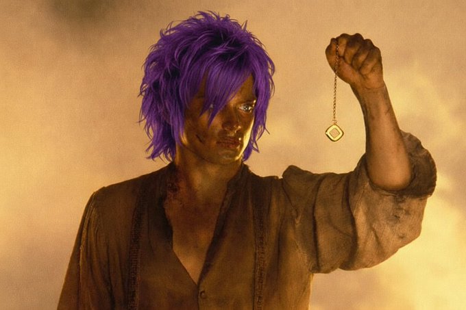 Digital artwork of a young man with purple hair, wearing a worn shirt, holding up a gold pocket watch on a chain against a hazy sky.