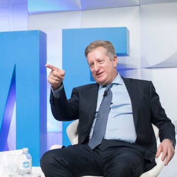 A man in a dark suit and tie sits on stage gesturing with his hand while speaking, with large blue letters visible in the background. The setting appears to be a financial or business conference, aligning with the post about investor Steve Eisman discussing AI and dismissing extinction fears on CNBC.