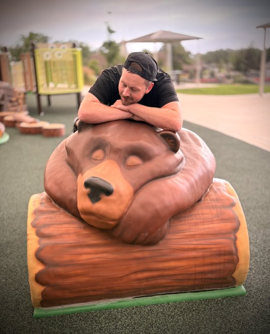 A man rests his head on a large sleeping bear statue at a playground, humorously illustrating the exhaustion and defeat of being on the wrong side of the market. The image ties to the post's "shorting the tops" joke by visually representing the feeling of being worn out and humbled by market movements in BTC, SUI, and SOL.
