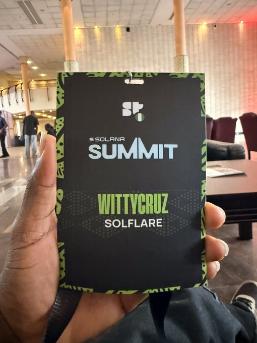 A hand holds a Solana Summit badge reading 'WITTYCRUZ / SOLFLARE' with an 'SF' logo, taken inside an event venue.