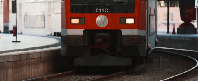 Front view of a red and gray train numbered '011C' with headlights on, traveling along curved tracks at a station platform.