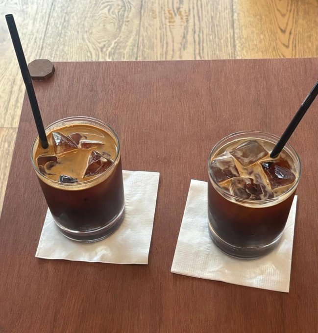 Two glasses of iced coffee with black straws sit on white napkins on a dark wooden table.