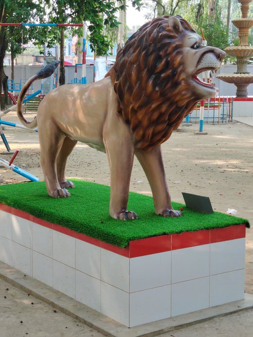 The image features a large statue of a lion standing on a white pedestal with red trim. The lion appears to be roaring or growling, adding an element of intensity to the scene. In the background, there are trees that provide a natural backdrop for the statue and pedestal. The caption above the image reads: "Good Morning with @useTria Technology becomes powerful when it removes complexity instead of adding more of it. That’s why I’m keeping a close eye on @useTria and @MindoAI". This suggests that there might be some connection between the lion statue and the technology being discussed in the caption, possibly related to the theme of simplification or the use of artificial intelligence for creative purposes.
