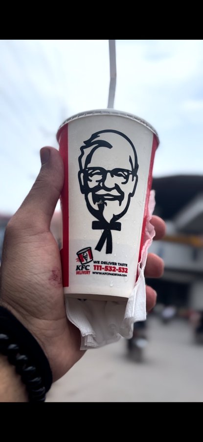 A hand holds a KFC drink cup displaying the Colonel Sanders logo and Turkish text reading 'İVE DELİVERİN TASTE' along with a phone number and website.