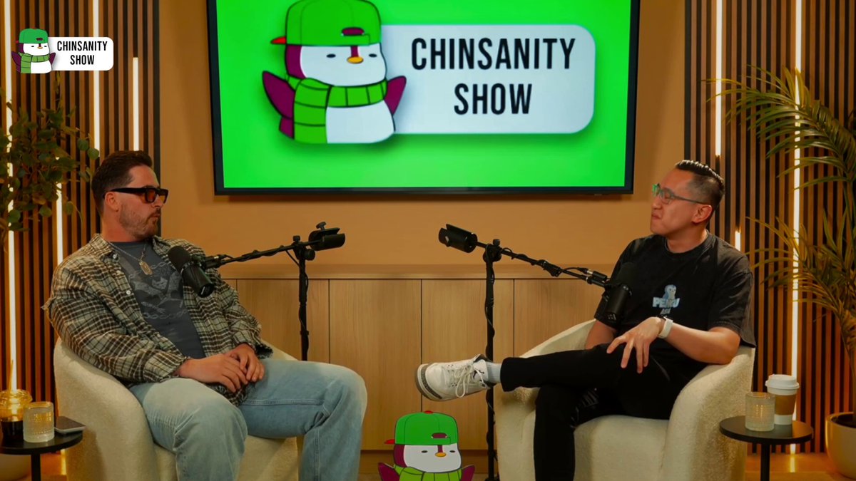 The image features two men sitting in chairs with microphones in front of them, appearing as hosts or guests at an event related to the "Chinsanity Show" podcast. The background includes a television screen displaying the show's logo and text, indicating that this is likely a live broadcast or a recording session.