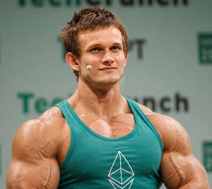 A muscular young man with short brown hair wearing a green Ethereum tank top and a headset microphone, appearing to be speaking at a TechCrunch event.