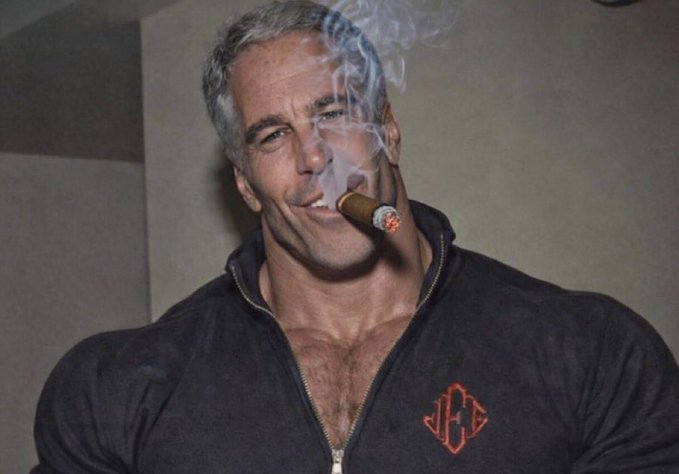 A man with short gray hair wearing an unzipped dark hoodie smokes a large lit cigar while looking at the camera.
