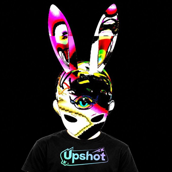 A digital illustration of a figure wearing a vibrant, colorful rabbit mask with one visible blue eye, and a black t-shirt with the 'Upshot' logo.