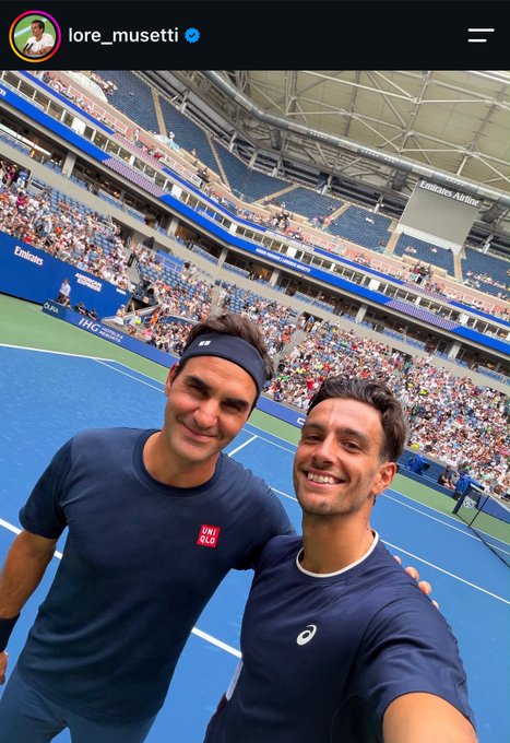 A selfie of tennis players Roger Federer and Lorenzo Musetti (username lore_musetti) smiling together on the court at the US Open, with "Emirates Airline" and "US Open" signage visible in the stadium behind them.