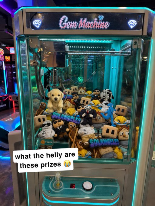 The post says: "play bullish games, win bullish prizes"

Caption: A "Gem Machine" claw machine is filled with plush prizes labeled "SOLANGELES," featuring mascots wearing sunglasses and suits—including dogs, miners, and figures styled like Bitcoin/crypto characters—tying into the post's theme of winning bullish crypto-themed prizes.