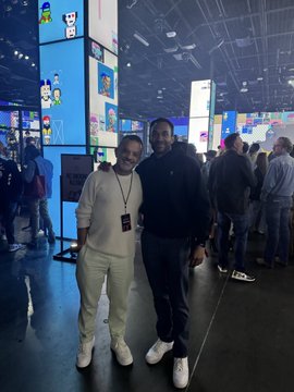 A photo shows a man and a woman smiling together at what appears to be a convention center, with brightly lit displays visible in the background.