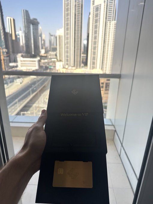 A hand holding an open VIP welcome folder with a gold card, with a city skyline of skyscrapers visible through a window in the background.