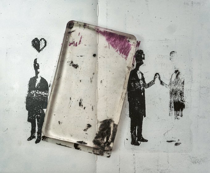 A weathered metal tray rests on a white surface printed with stenciled figures of people, including one with a heart above their head and two others shaking hands.