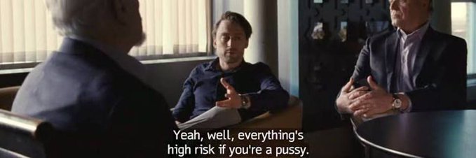A movie scene showing two men in a serious conversation, with subtitles reading 'Yeah, well, everything's high risk if you're a pussy.'