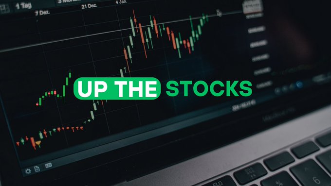 A laptop screen displays a green and red candlestick stock chart with the overlay text "UP THE STOCKS," visually promoting a new stocks and shares channel that tracks a journey to grow £500 into £100,000 through stock and crypto investments.
