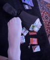 The image shows a person's foot with white socks, standing next to a black surface that has various items scattered around it. The objects include a wallet, a cell phone, some papers, and several small packages or envelopes. One of these packages contains pizza slices, suggesting that someone might have been enjoying a meal nearby. The post appears to be about sharing pizza with others, as indicated by the use of the hashtag #okx.