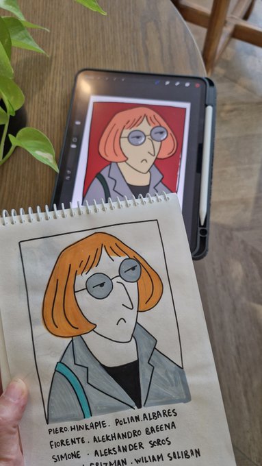 A hand holds a spiral notebook featuring a hand-drawn portrait that closely matches a digital reference image displayed on a tablet behind it.