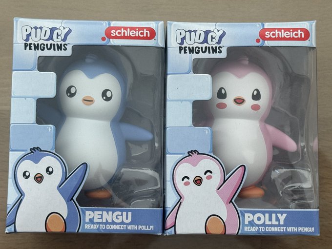 Two boxed Schleich 'Pudgy Penguins' collectible figurines side by side: a blue penguin labeled 'PENGU READY TO CONNECT WITH POLLY!' and a pink penguin labeled 'POLLY READY TO CONNECT WITH PENGU!'.