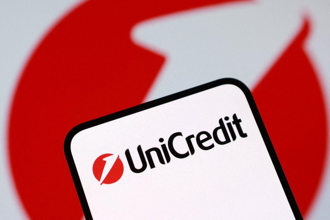 The UniCredit bank logo is displayed on a smartphone screen against a red and white background featuring the company's larger emblem, representing Italy's second-largest bank as it explores crypto trading and custody services.