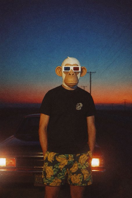 The image features a man wearing a monkey mask, standing next to a car with his hands in his pockets. He is also wearing shorts that have bananas printed on them. The background of the photo shows an orange sky at sunset, which adds a warm and vibrant atmosphere to the scene. The caption "GM whatever your time zone bored ape yacht club" suggests that the man's attire and the setting are related to a theme or event involving monkeys and cars.