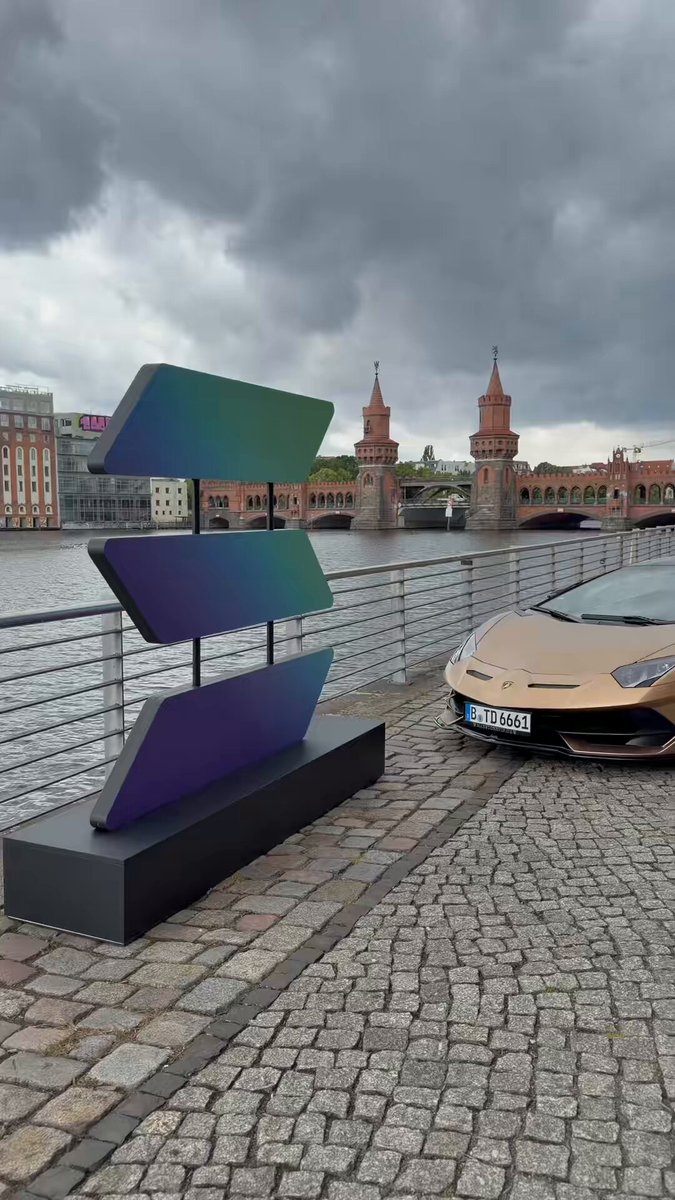 The image features a car parked next to a large, colorful sculpture of three arrows pointing in different directions. The sculpture is located near a body of water with a bridge visible in the background. The car appears to be a sports car, adding an element of luxury and style to the scene. The post about web3 seems unrelated to the image but might have been included as part of the content or for promotional purposes.