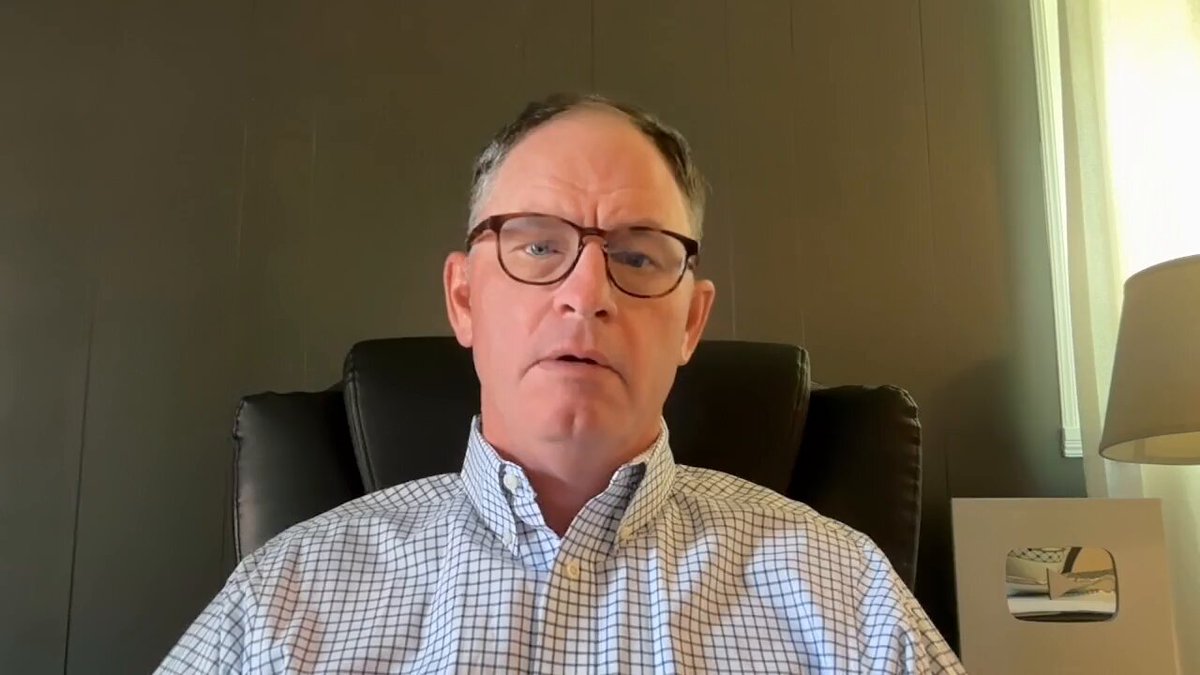 The image shows a man wearing glasses sitting in an office chair, looking at the camera with a serious expression. Behind him, there is a lamp that appears to be turned off or dimmed. The background of the image features a wall painted in shades of gray and brown. The caption for the image reads "XRP Perfect Storm Watch The Full Youtube Video Here: youtu.be/6yfTOk9FjCQ".