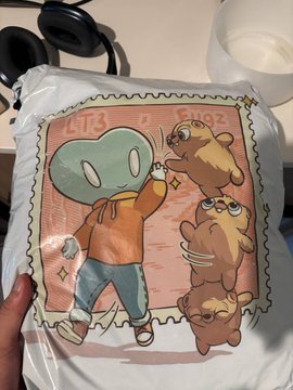 A t-shirt in plastic packaging featuring an illustration of Squidward from SpongeBob SquarePants surrounded by three brown bears on a postage stamp design.