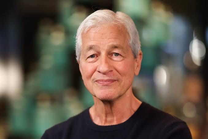 A portrait of an older man with gray hair wearing a black t-shirt against a blurred green background.