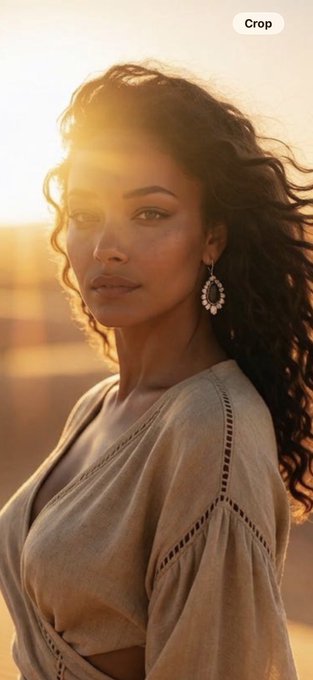 A portrait of a woman with curly dark hair wearing a beige v-neck top and ornate earrings, photographed during golden hour with a 'Crop' button visible.