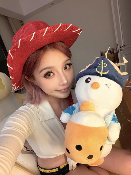 A young woman with pink hair wearing a red cowboy hat poses with a cute plush snowman character dressed in a navy blue hat featuring the Kung Fu Tea 功夫茶 logo, promoting the collaboration between pudgypenguins and Kung Fu Tea. The plush appears to be the "Fat Penguin" character being featured in the co-branded milk tea partnership.