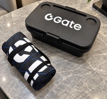 A rolled-up black patterned towel or wrap with blue and white designs sits next to a black plastic case branded with 'cGATE' in white letters on a marble countertop.