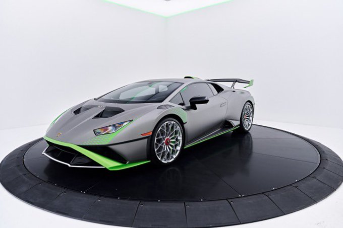 A sleek gray Lamborghini Huracán STO with vibrant green accents is displayed on a rotating platform in a showroom, representing one of this week's client pickups paid for in full with crypto.