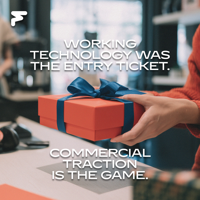An orange gift box with a dark blue ribbon is handed across a desk, overlaid with the text "WORKING TECHNOLOGY WAS THE ENTRY TICKET. COMMERCIAL TRACTION IS THE GAME."

The image visually reinforces the post's message by metaphorically representing the handoff from building technology to packaging it as a product ready for market—much like wrapping a gift for delivery, the focus has shifted from creating the tech to presenting and commercializing it for buyers.