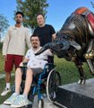 A woman in a wheelchair poses next to a horse statue, flanked by two men, in what appears to be a casual outdoor photo to accompany a cryptocurrency airdrop promotion for $ANSEM.