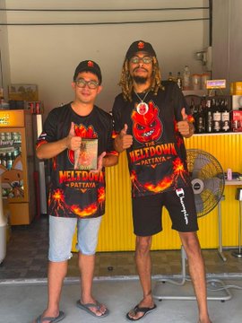 Two men pose wearing matching black 'Meltdown Pizza' flame-patterned shirts and caps, standing in what appears to be a restaurant or shop interior.