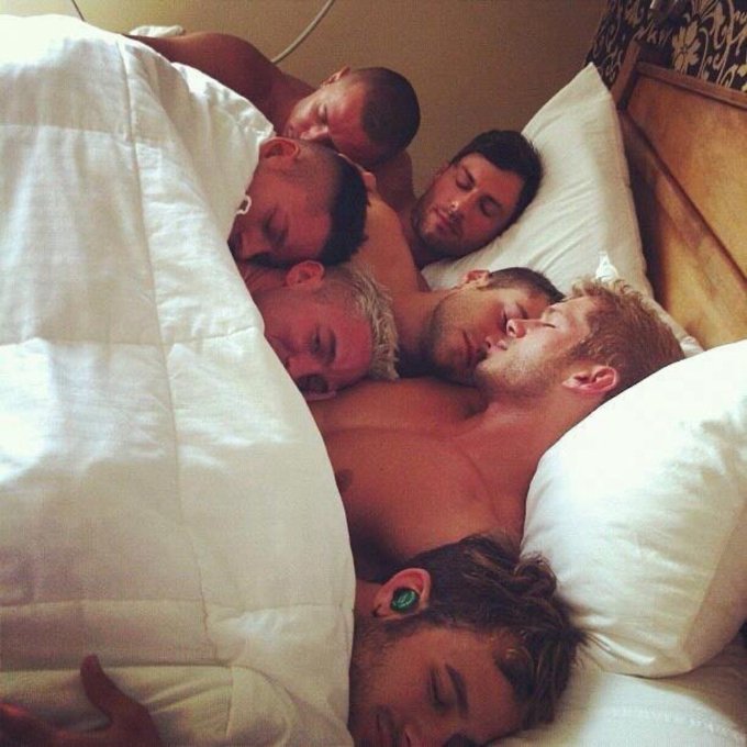 Several shirtless young men are crowded together sleeping in a bed with white pillows and bedding, their bodies tangled as they rest.

The image humorously illustrates the post's joke about cryptocurrency "insiders" who rug-pull coins for millions—the peaceful, exhausted slumber of multiple people in one bed visualizes the implied group of co-conspirators casually catching sleep after pulling off a massive financial scam.