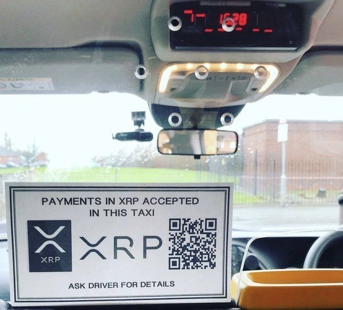 A sign inside a taxi reading 'PAYMENTS IN XRP ACCEPTED IN THIS TAXI' with the XRP logo and a QR code, asking customers to 'ASK DRIVER FOR DETAILS'.