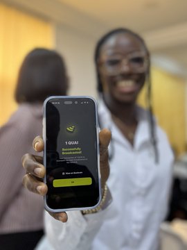 A smiling woman proudly holds up her phone displaying the BlipPay app with a "Successfully created account" message, celebrating new user sign-ups at the Money Moves event in Uyo with the Quai community in Nigeria.