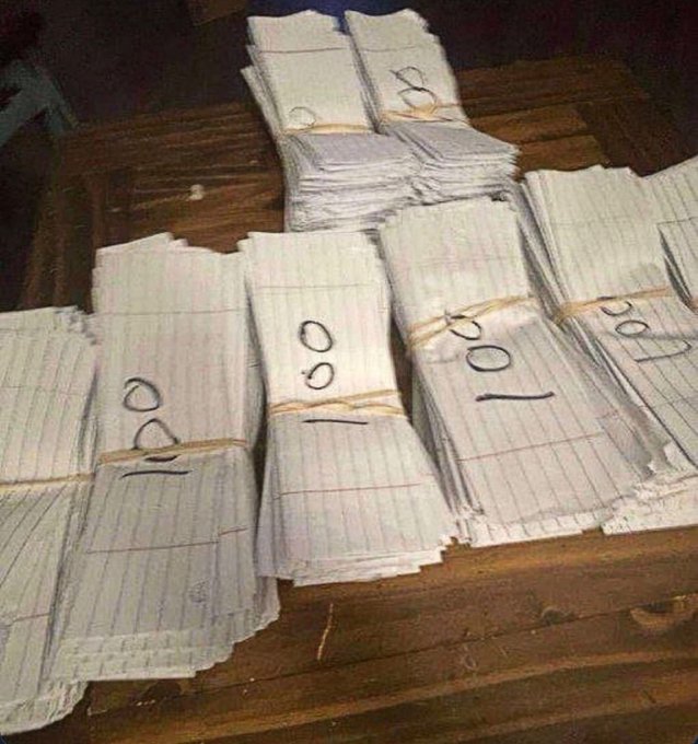 Bundles of lined paper marked "50," "100," and "150" are stacked on a wooden surface, humorously representing large sums of money in a makeshift way that ties into the post's theme of manifesting crypto profits by using fake money as a visual stand-in for wealth gains.