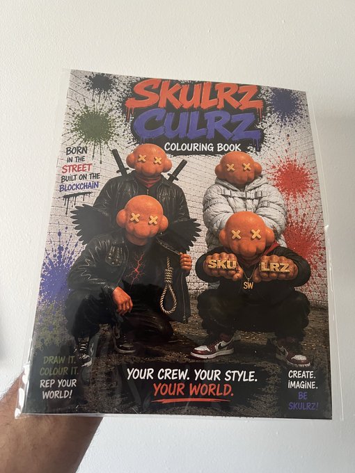 A hand holds up a 'SKULRZ CULRZ COLOURING BOOK' featuring characters in streetwear and pumpkin masks with 'X's for eyes, accompanied by text like 'BORN IN THE STREET', 'BUILT ON THE BLOCKCHAIN', and 'YOUR CREW. YOUR STYLE. YOUR WORLD.'