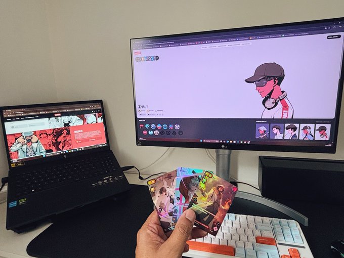 The image features a person holding two cards over a computer monitor displaying a cartoon character. The scene takes place next to an open laptop, which has a website displayed on its screen. The person's hand holds one of the cards, while the other card is placed in front of them. The background shows a wall with a TV mounted above it and another TV positioned below it.
