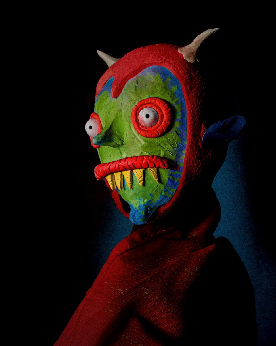 The image features a mask with a face, painted in red, green, blue, yellow, and white colors. The mask appears to be made of clay or plaster, giving it an artistic and unique appearance. The background is black, which contrasts with the colorful mask and draws attention to its details. The post includes text that reads "Objkt collection Day #76 Maybe I'LL SEE YOU TOMORROW?". This suggests a connection between the mask's creation and the upcoming event or occasion it might be related to.