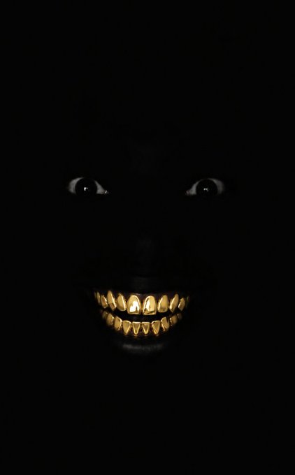 A dark, eerie image showing only a pair of glowing eyes and a menacing gold-toothed smile emerging from pitch-black shadows.