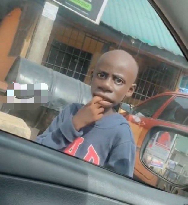 A young boy in a blue sweatshirt looks thoughtfully out a car window with his hand on his chin.